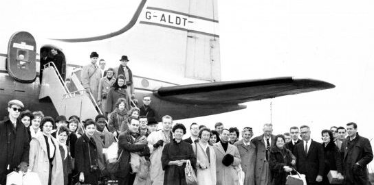 Members of the Eastman Philharmonia gather for a photo in front of the tail section of a Hermes IV airplane after deplaning.Members of the Eastman Philharmonia gather for a photo in front of the tail section of a Hermes IV airplane after deplaning.
