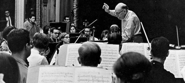 Igor Stravinsky conducts an Eastman ensemble on stage in Eastman Theatre during a weeklong residency at Eastman (March 1966). Photograph from ESPA 24/48 (8x10). Igor Stravinsky conducts a student orchestra on the Eastman Theatre stage, viewed from the 3rd row of the 2nd violin section.