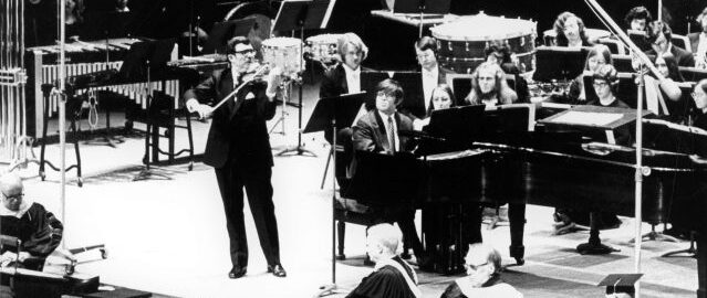 Zvi Zeitlin and Robert Freeman perform at Mr. Freeman’s inauguration in the Eastman Theatre (1973). Photograph from ESPA 37/18A. Zvi Zeitlin, violin, and Robert Freeman, piano, perform on the Eastman Theatre stage, with a student ensemble seated in the background.