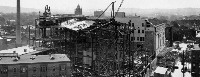 Black and white photo of the construction of Eastman Theatre, showing the building's steel structure as viewed from the roof of the YMCA building on Gibbs Street. Black and white photo of the construction of Eastman Theatre, showing the building's steel structure as viewed from the roof of the YMCA building on Gibbs Street.