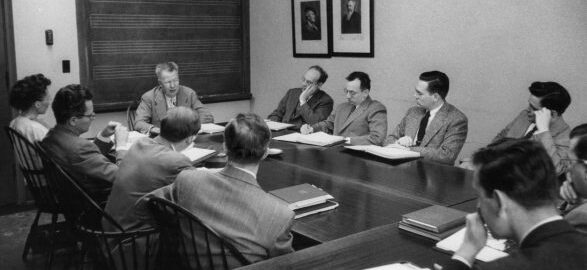 Harold Gleason instructs a class of 10 students, all seated around a seminar table, at the Eastman School of Music.