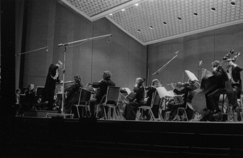 R1397-18 Eastman Philharmonia concert that featured the premiere of Krzystof Penderecki’s Partita for Harpsichord and Orchestra. At the conclusion of the Partita, Maestro Hendl invites the composer to the stage for bows. In the last shot, the composer, the soloist, and the conductor all join hands to acknowledge the applause.