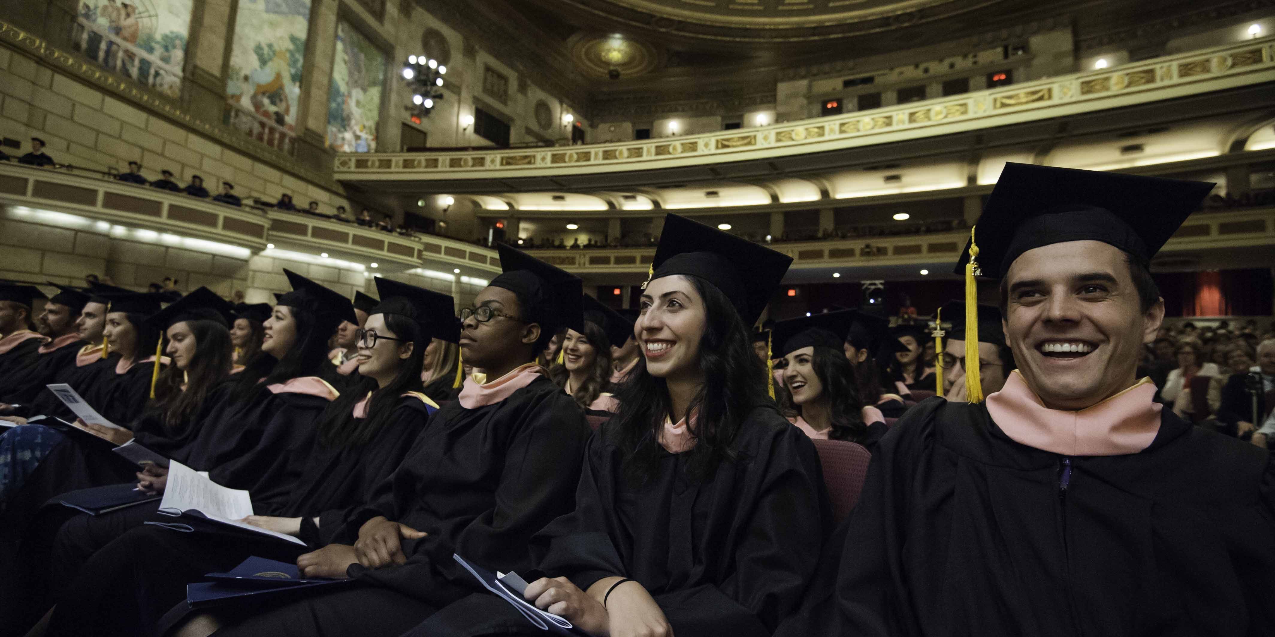 A row of smiling students in graduation caps and gowns in the theater.