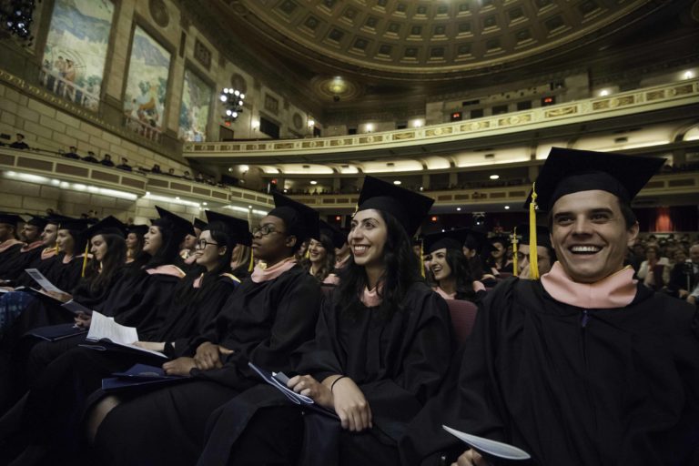 Commencement 2015 students Listening A row of smiling students in graduation caps and gowns in the theater.