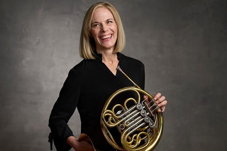woman in black shirt, holding french horn.