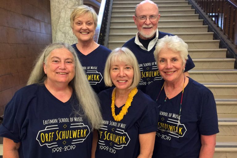 Five faculty members in dark blue T-shirts standing on staircase in Lowry Hall.