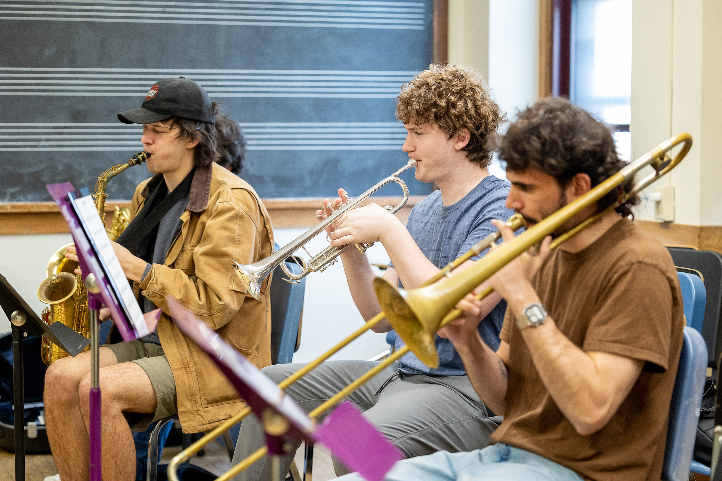 Three students playing brass instruments in classroom