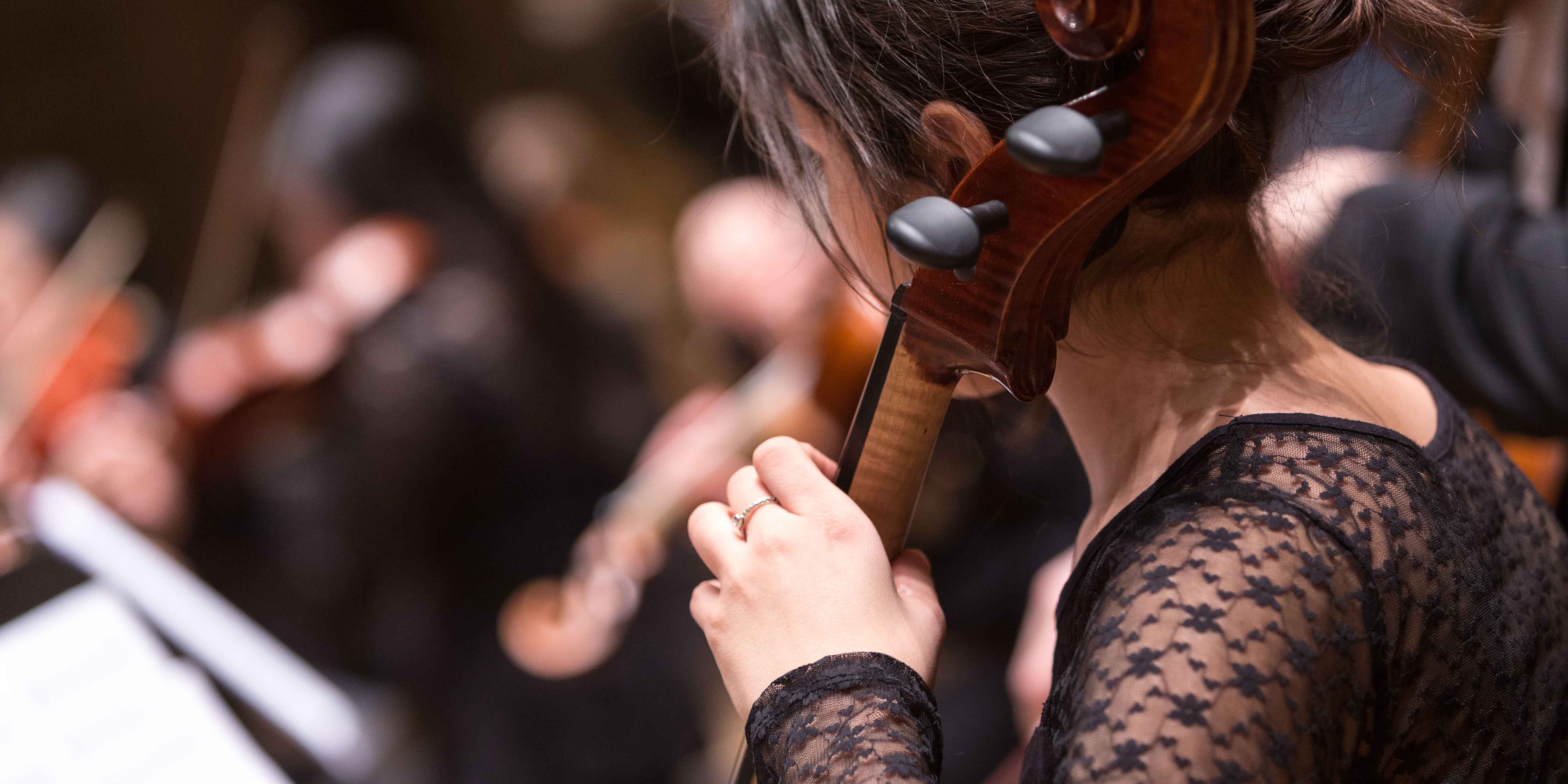 Musicians Unite to Benefit Rochester’s Foodlink A woman in a black dress playing cello in an orchestra setting.